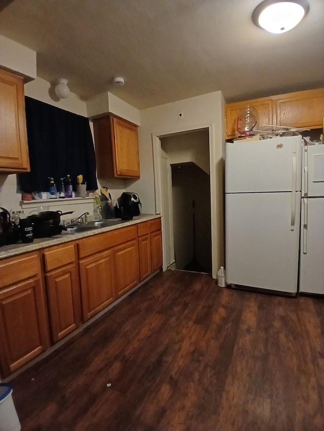 kitchen featuring dark wood-style floors, brown cabinetry, a sink, and freestanding refrigerator