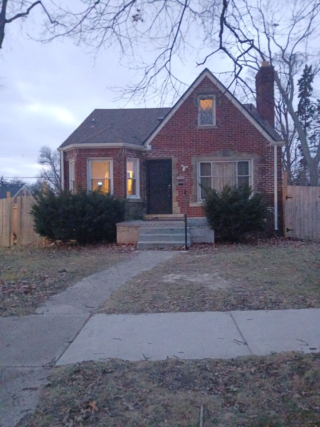 view of front facade with brick siding, a chimney, and fence