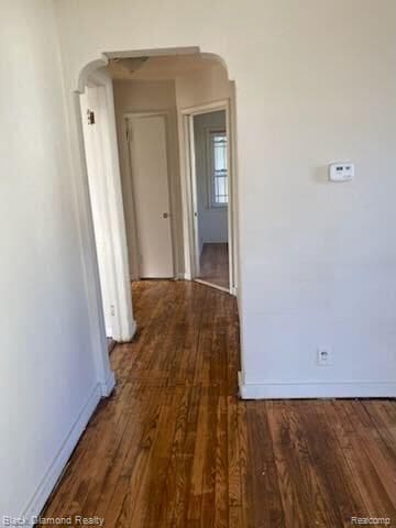 hallway with baseboards, arched walkways, and wood finished floors