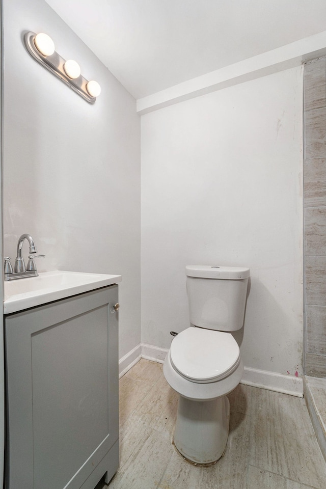 bathroom featuring toilet, baseboards, wood finished floors, and vanity