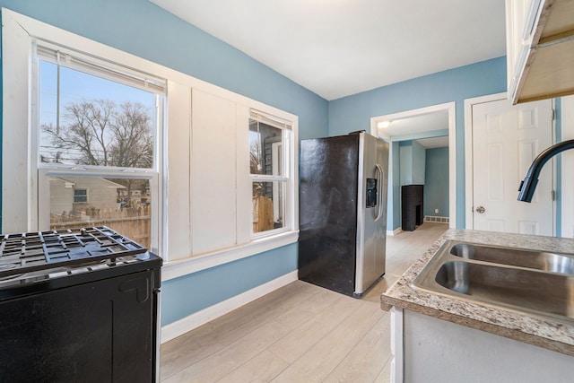 kitchen featuring stainless steel fridge, baseboards, black range with gas stovetop, light wood-style floors, and a sink