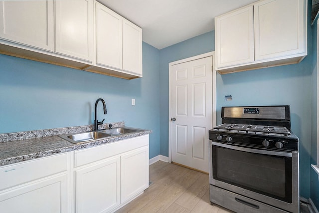 kitchen featuring stainless steel range with gas cooktop, light wood finished floors, white cabinets, a sink, and baseboards