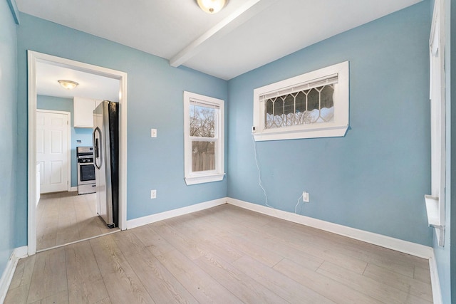 unfurnished room featuring light wood-type flooring, baseboards, and beam ceiling