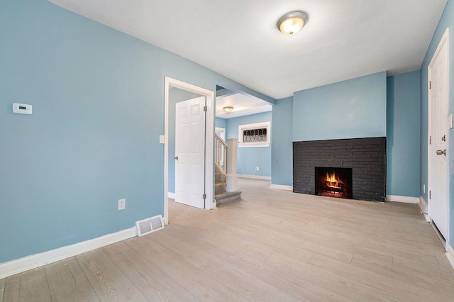 unfurnished living room with baseboards, visible vents, wood finished floors, stairs, and a brick fireplace