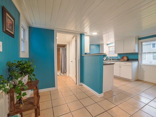 kitchen featuring dark countertops, white cabinets, light tile patterned flooring, wooden ceiling, and baseboards