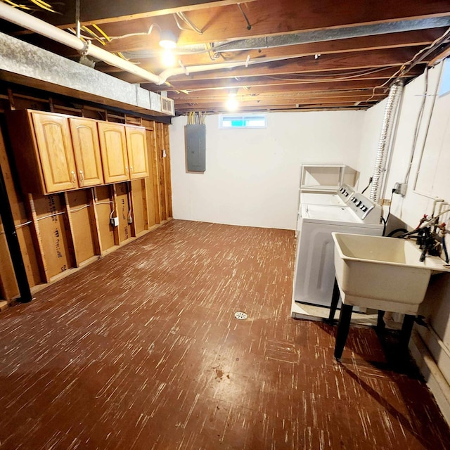 basement featuring washing machine and dryer, electric panel, dark wood-style flooring, and a sink