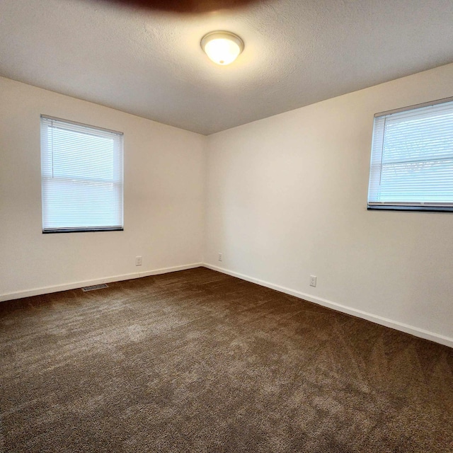 spare room featuring baseboards, dark carpet, and a textured ceiling