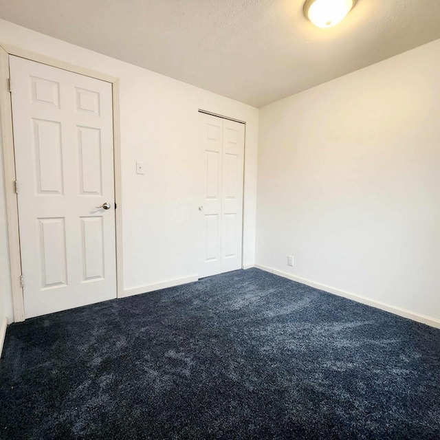 unfurnished bedroom featuring a closet, dark carpet, and baseboards