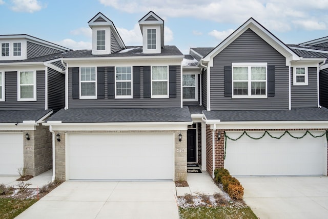 multi unit property with a garage, driveway, a shingled roof, and stone siding