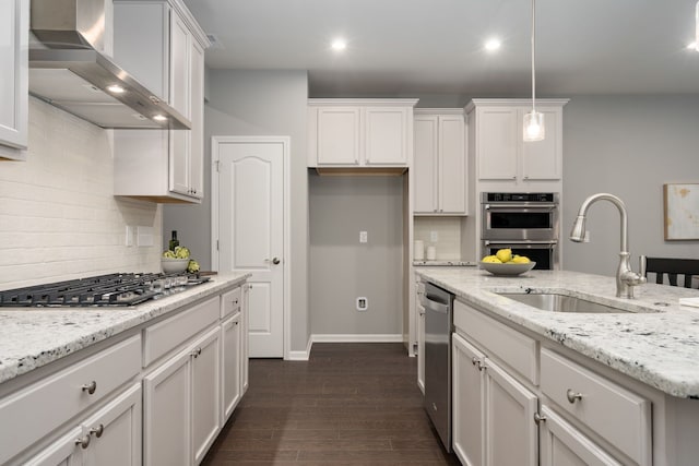 kitchen with dark wood-style flooring, stainless steel appliances, white cabinetry, a sink, and wall chimney exhaust hood