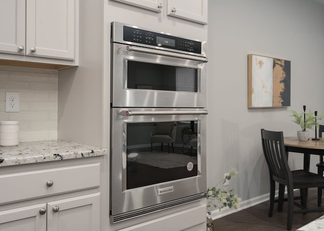 kitchen featuring tasteful backsplash, baseboards, light stone countertops, stainless steel double oven, and white cabinetry