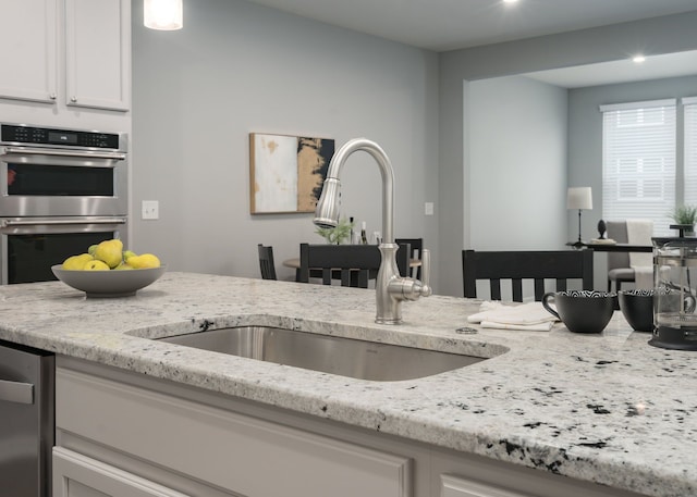 kitchen with stainless steel appliances, light stone counters, a sink, and white cabinets