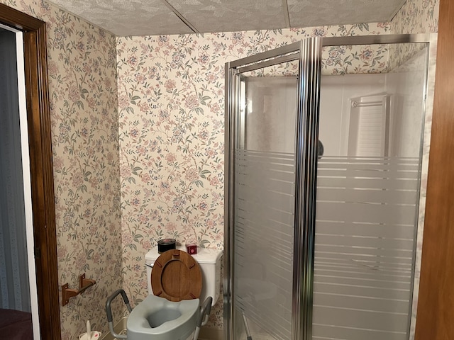 bathroom with toilet, wallpapered walls, a textured ceiling, and a stall shower