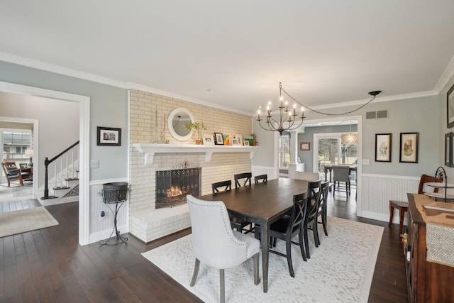 dining area with a brick fireplace, a wainscoted wall, dark wood-style floors, and visible vents