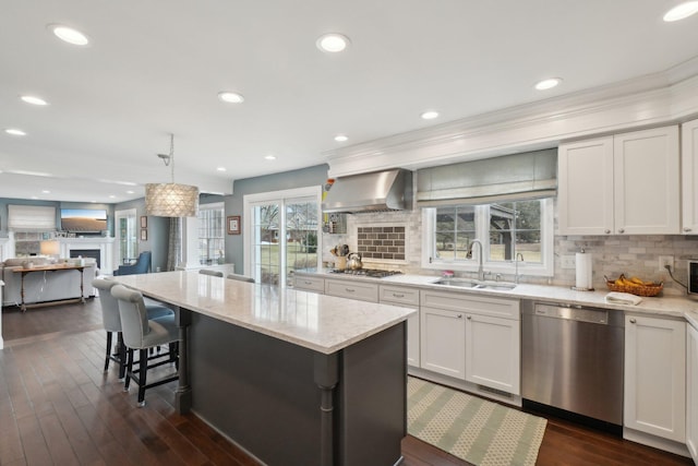 kitchen featuring plenty of natural light, light stone counters, stainless steel appliances, wall chimney range hood, and a sink