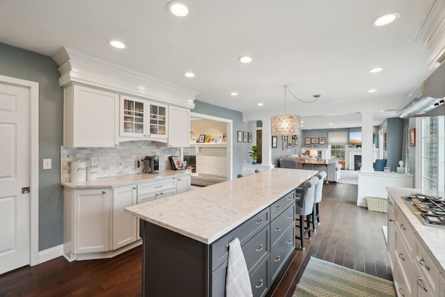 kitchen featuring decorative backsplash, a kitchen island, glass insert cabinets, a lit fireplace, and white cabinetry