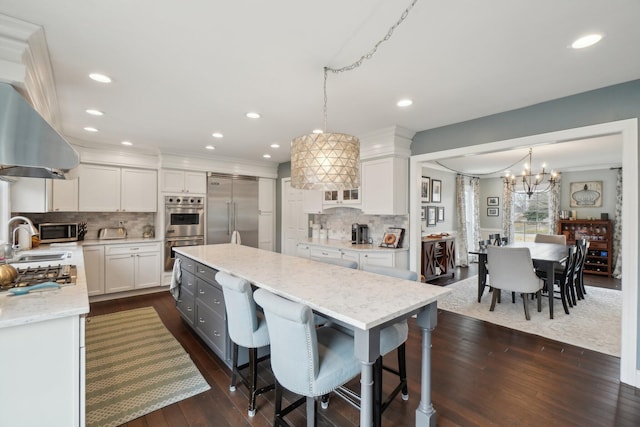 kitchen featuring white cabinets, dark wood finished floors, a kitchen island, appliances with stainless steel finishes, and a breakfast bar