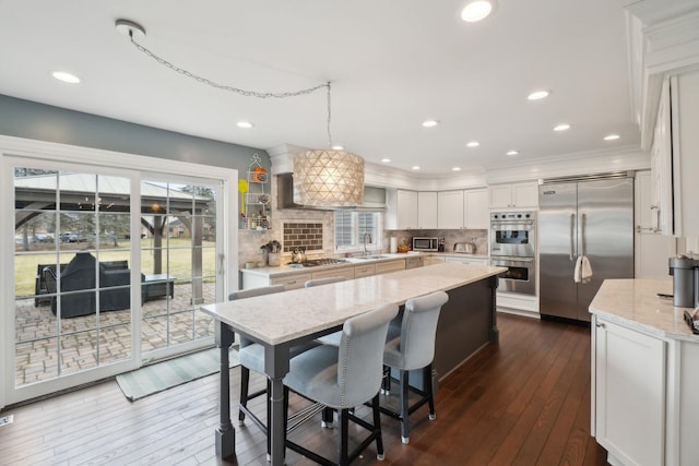 kitchen with decorative backsplash, white cabinets, a kitchen island, appliances with stainless steel finishes, and a sink