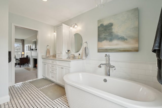 bathroom featuring a warm lit fireplace, double vanity, and a freestanding tub