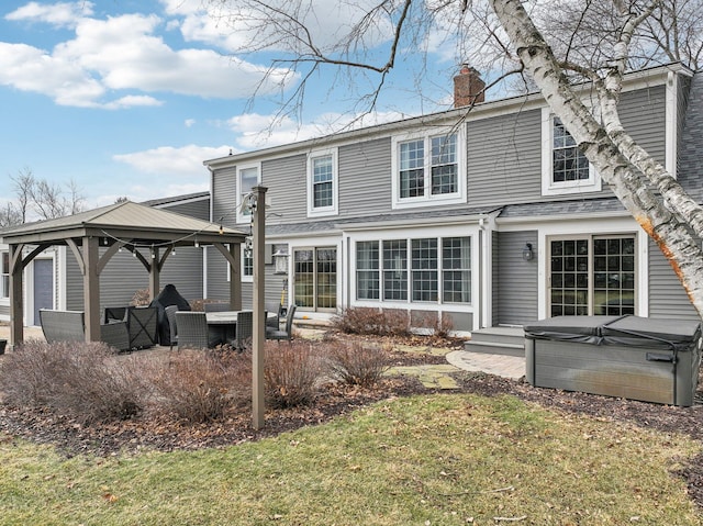 back of house with a chimney, a lawn, a hot tub, and a gazebo