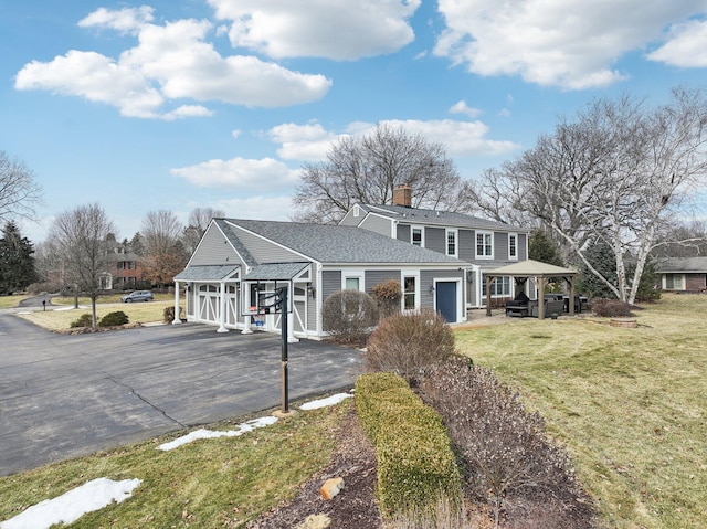 view of front of property with a chimney, aphalt driveway, a front lawn, and an attached garage