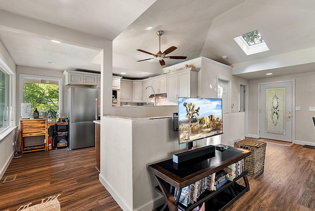 kitchen featuring a peninsula, dark wood finished floors, baseboards, lofted ceiling with skylight, and stainless steel fridge