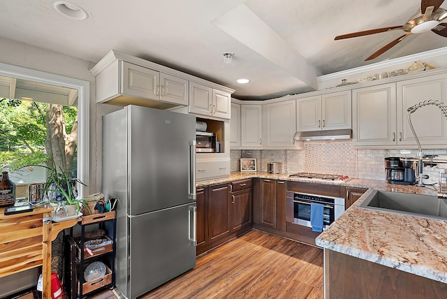 kitchen with stainless steel appliances, tasteful backsplash, light wood-style floors, light stone countertops, and under cabinet range hood