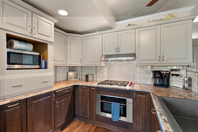 kitchen with stainless steel appliances, decorative backsplash, dark brown cabinets, wood finished floors, and under cabinet range hood