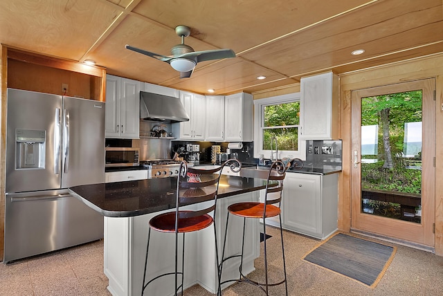 kitchen with stainless steel appliances, dark countertops, backsplash, white cabinets, and wall chimney range hood