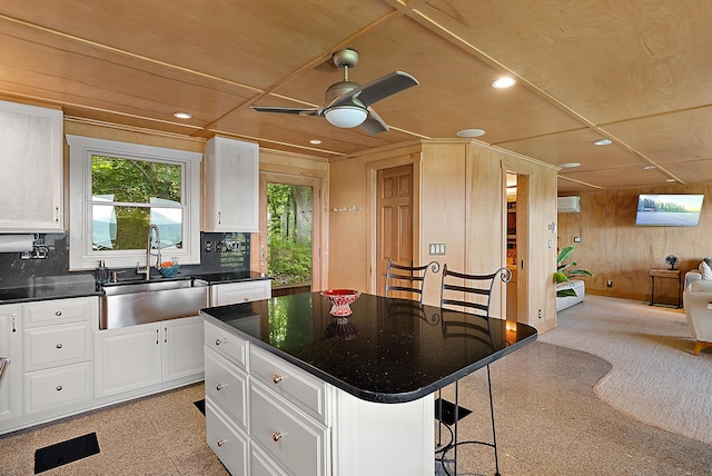 kitchen featuring dark countertops, open floor plan, white cabinetry, a sink, and wood walls