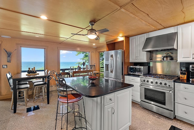 kitchen featuring a water view, white cabinetry, appliances with stainless steel finishes, wall chimney exhaust hood, and dark countertops