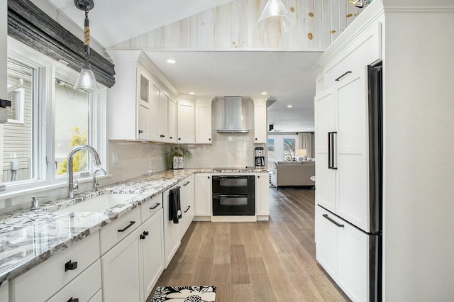 kitchen featuring white cabinets, wall chimney exhaust hood, a sink, light wood-style floors, and backsplash