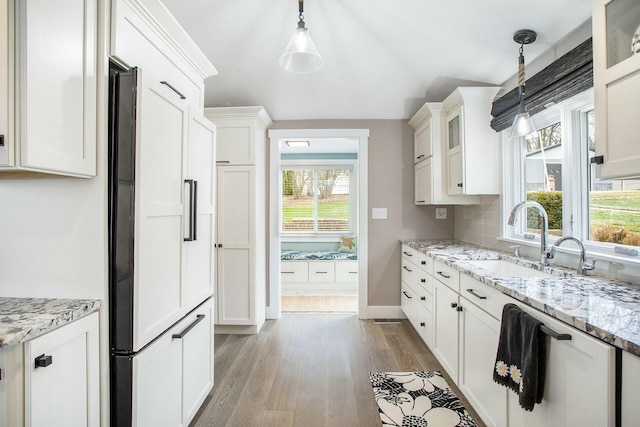 kitchen featuring tasteful backsplash, light wood-style flooring, glass insert cabinets, white cabinets, and a sink