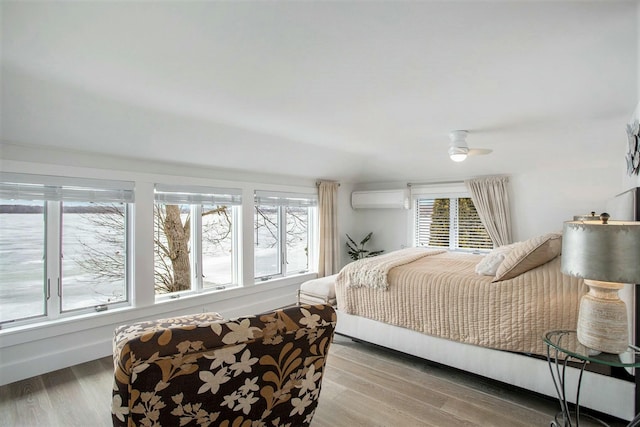 bedroom with wood finished floors, a wall mounted air conditioner, and multiple windows