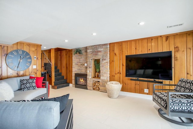 living area featuring recessed lighting, visible vents, stairway, wood walls, and a stone fireplace