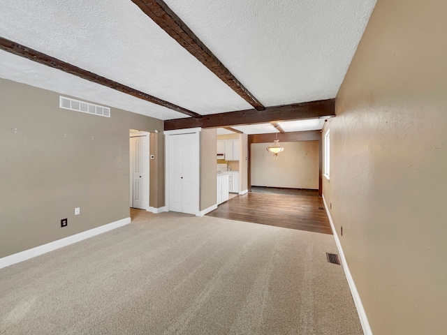 unfurnished living room featuring beam ceiling, visible vents, and a textured ceiling