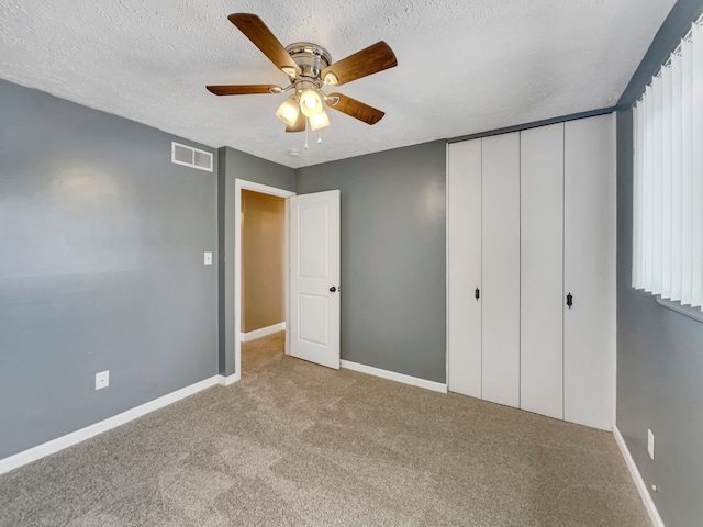 unfurnished bedroom with a textured ceiling, visible vents, baseboards, a closet, and carpet