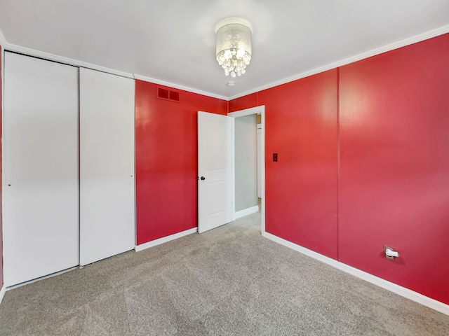 unfurnished bedroom featuring baseboards, visible vents, ornamental molding, carpet floors, and a closet