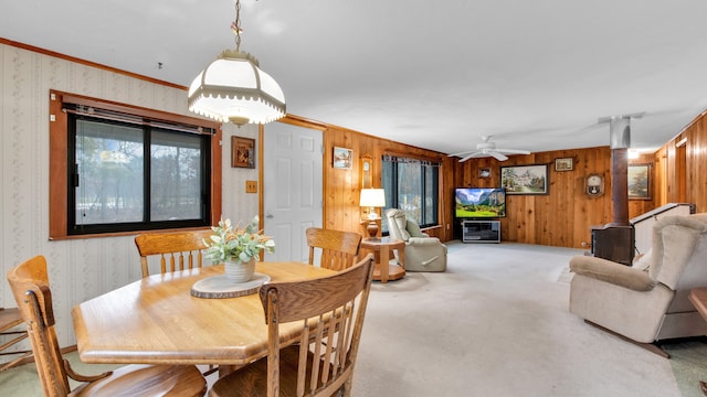 dining space with ceiling fan, a wood stove, light colored carpet, and wallpapered walls