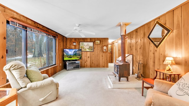 living room with ceiling fan, wooden walls, a wood stove, and light colored carpet