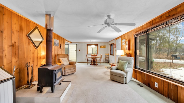 living area with a wood stove, light colored carpet, wood walls, and visible vents