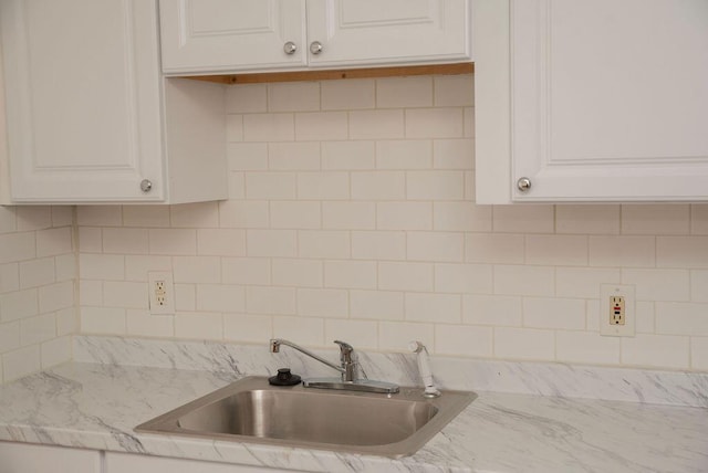 kitchen featuring light stone countertops, tasteful backsplash, white cabinetry, and a sink