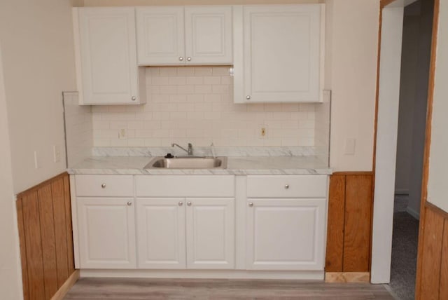 kitchen featuring white cabinets, light countertops, a sink, and wainscoting