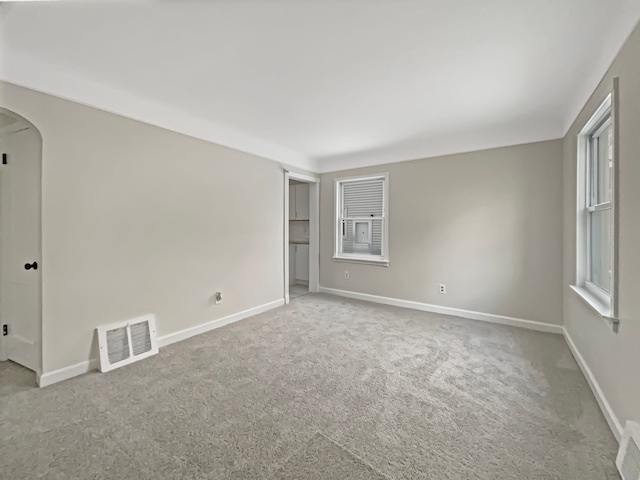 carpeted empty room with baseboards, visible vents, and arched walkways