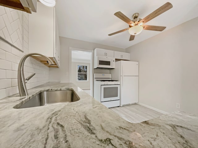 kitchen featuring tasteful backsplash, white cabinets, a sink, light stone countertops, and white appliances