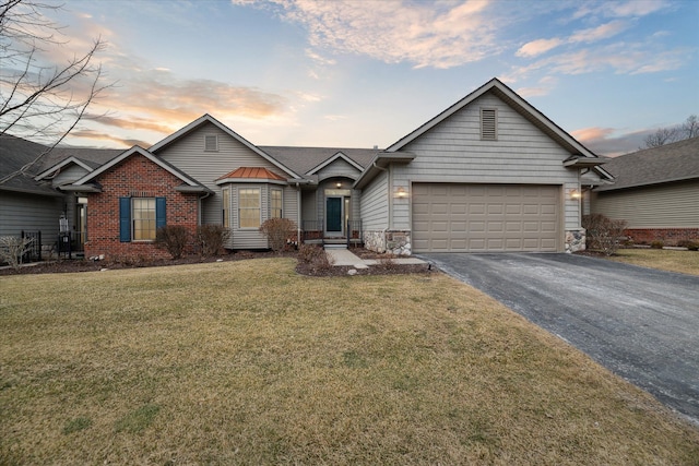 view of front of property with an attached garage, brick siding, aphalt driveway, and a yard