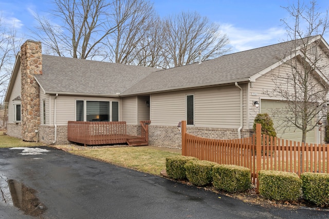 ranch-style house with brick siding, a chimney, a shingled roof, an attached garage, and fence