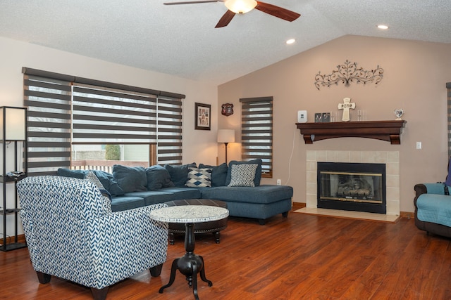 living area featuring ceiling fan, vaulted ceiling, a textured ceiling, wood finished floors, and a tile fireplace