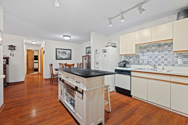 kitchen with tasteful backsplash, white appliances, dark wood-type flooring, and a sink