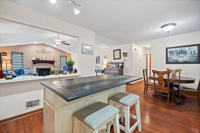 kitchen featuring dark wood-style flooring, lofted ceiling, visible vents, a tiled fireplace, and a textured ceiling